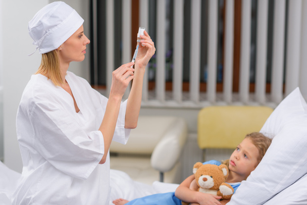 médico femenino que prepara la vacunación para el niño enfermo
 - Foto, Imagen
