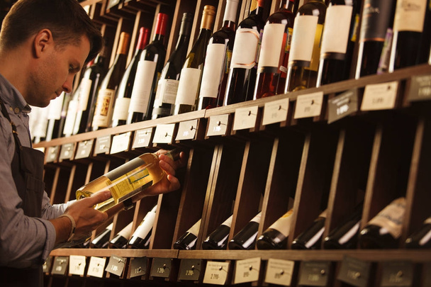 Thoughtful expert in winemaking on background of shelves with wine. - Foto, imagen