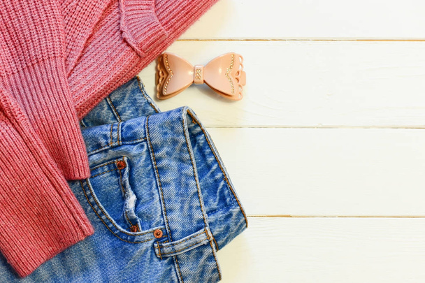 Γυναικεία casual ένδυσης. Γυναικών μπλε τζιν, το ροζ πλεκτό πουλόβερ, φουρκέτα σε φόντο ξύλινη με αντίγραφο χώρο για το κείμενο. Το Top view. Χαριτωμένο casual ντύσιμο. Casual ντύσιμο για το έργο. Ιδέα της casual ντύσιμο με jeans. Casual wear για κυρίες - Φωτογραφία, εικόνα
