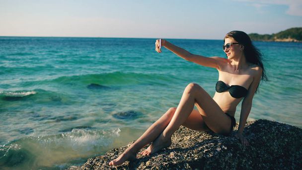 Mulher bonita tomando selfie usando telefone na praia sorrindo e gostando de viajar estilo de vida em férias
 - Foto, Imagem