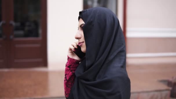 Young attractive woman wearing hijab walking in the street in city talking on her mobile phone. Slowmotion shot - Felvétel, videó