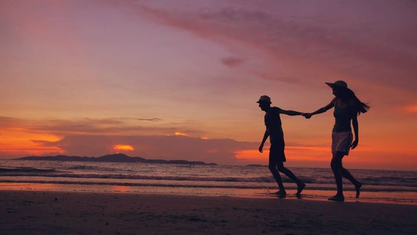 Силуэт счастливой влюбленной пары встречается и играет на пляже на закате океана
 - Фото, изображение
