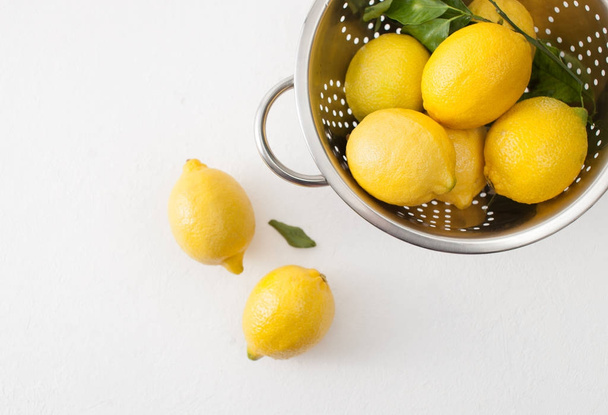 Fresh lemons with leaves in a colander on a white concrete background. - Фото, зображення