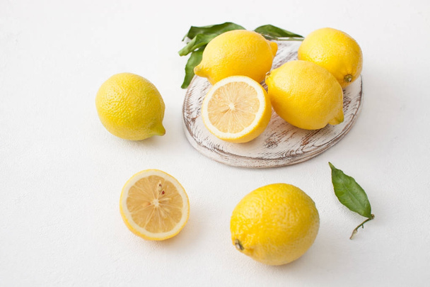 A bunch of lemons with leaves and sliced lemons on a white concrete background. - Φωτογραφία, εικόνα