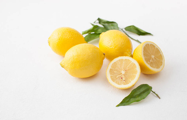 A bunch of lemons with leaves and sliced lemons on a white concrete background. - Foto, Imagem