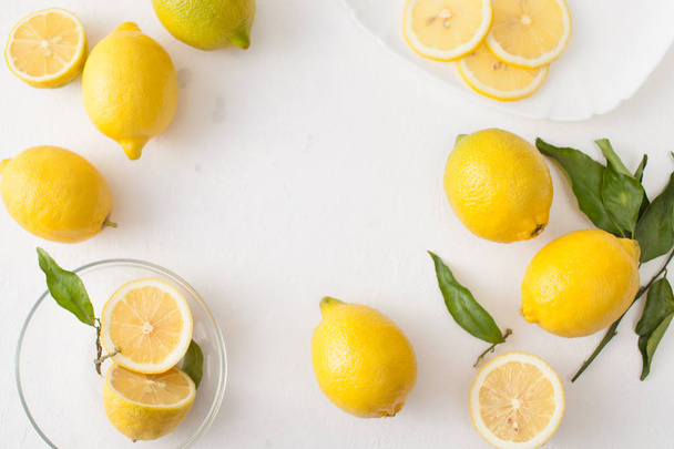 A bunch of lemons with leaves and sliced lemons on a white concrete background. - Photo, image