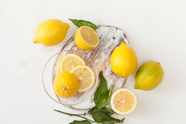 A bunch of lemons with leaves and sliced lemons on a white concrete background. - Fotografie, Obrázek