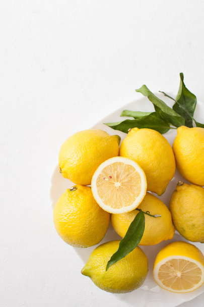 A bunch of lemons with leaves and sliced lemons on a white concrete background. - Foto, immagini