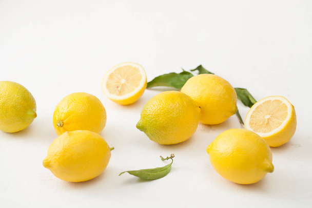 A bunch of lemons with leaves and sliced lemons on a white concrete background. - Φωτογραφία, εικόνα