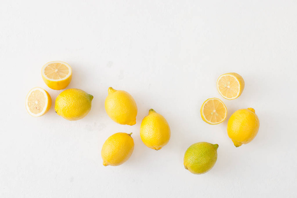 A bunch of lemons and cut lemons on a white concrete background. - Foto, afbeelding