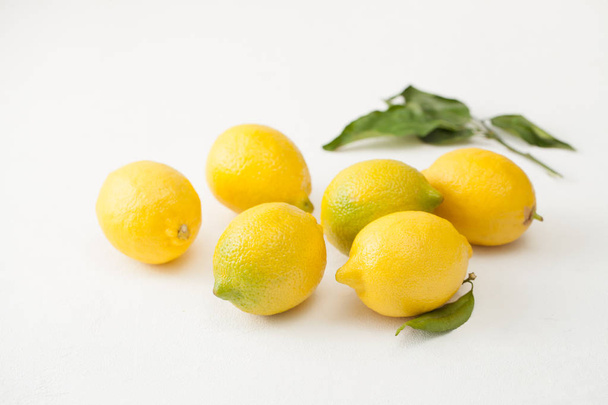 A bunch of lemons with leaves and sliced lemons on a white concrete background. - Фото, зображення