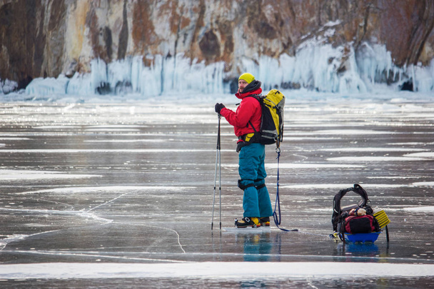 człowiek z plecaka przechodzi z powierzchni wody lodowej i wzgórza na tle, Rosja, jezioro Bajkał - Zdjęcie, obraz