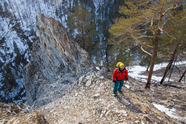 man with backpack stand on slope of rock with trees on foot, Russia, Lake Baikal - Fotoğraf, Görsel