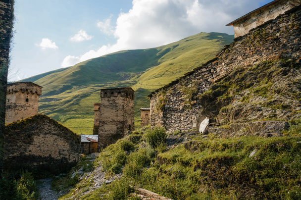 view of grassy field with old weathered rural buildings and hills on background, Ushguli, svaneti, georgia - Foto, Bild