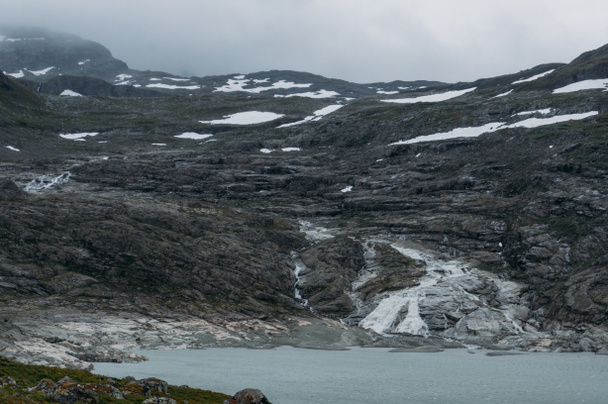 lake on foot of rock with snow on surface, Norway, Hardangervidda National Park - Foto, imagen