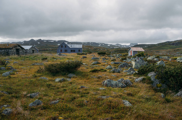 Nézd a zöld fű és a szétszórt kövekkel, szemben a kis falusi házak, Norvégia, Hardangervidda Nemzeti Park területén - Fotó, kép