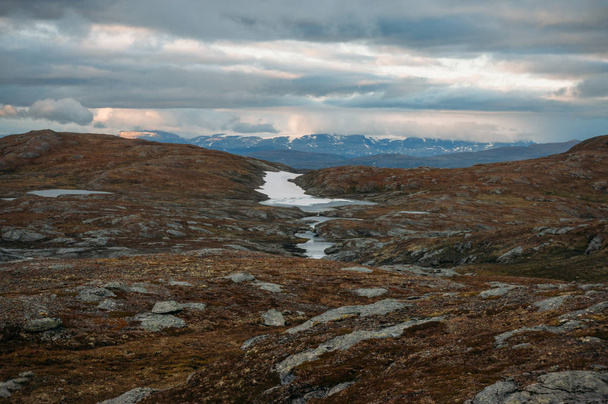 campo com pequenas lagoas de água e montanhas no fundo durante o tempo tempestuoso, Noruega, Hardangervidda National Park
 - Foto, Imagem