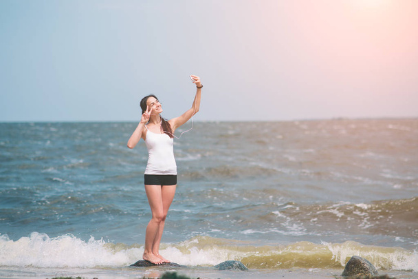 Fitness women exercising and stretching on the seacoast and making selfie - 写真・画像