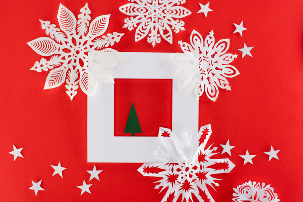 christmas tree in white frame with stars and paper snowflakes around, isolated on red   - Photo, image