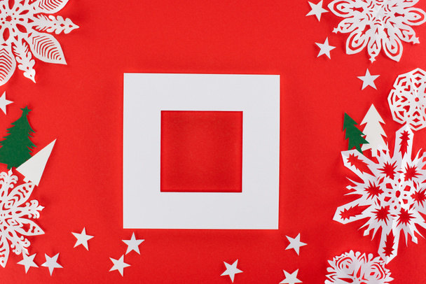 weißer Rahmen mit Weihnachtsbäumen, Sternen und Papierschneeflocken ringsum, isoliert auf rot   - Foto, Bild