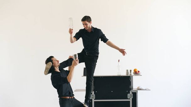 Профессиональный бармен жонглирует бутылками и коктейлями за столом мобильного бара на белом фоне студии в помещении
 - Фото, изображение