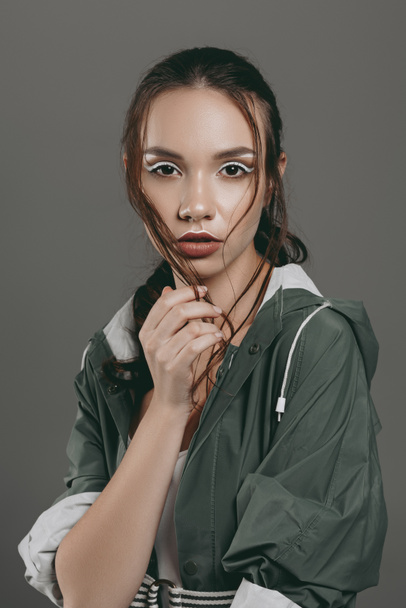 attractive girl with makeup posing in trendy raincoat, isolated on grey - 写真・画像