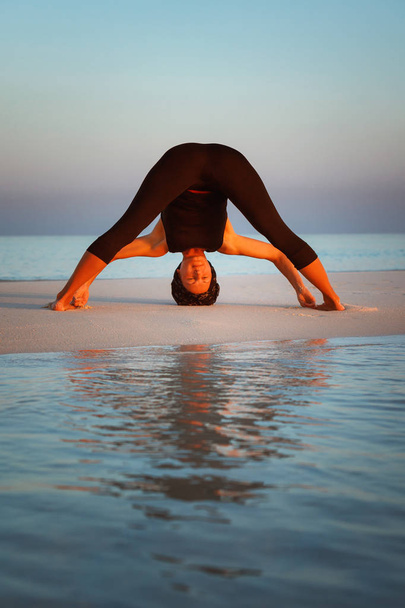 Summer yoga session on a beautiful golden beach of Wide-Legged Forward Bend - Prasarita Padottanasana I - Zdjęcie, obraz