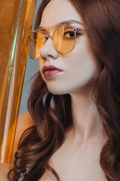 όμορφη αισθησιακό κορίτσι που θέτουν σε κίτρινα γυαλιά ηλίου, απομονώνονται σε γκρι - Φωτογραφία, εικόνα