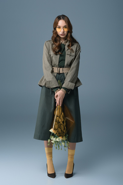 стильная девушка позирует в осеннем наряде с букетом цветов, изолированный на сером
 - Фото, изображение