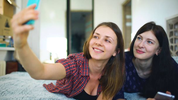 Happy cheerful sisters making selfie in morning and have fun on bed in bedroom at home - Fotoğraf, Görsel