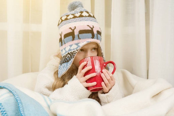 The season of autumn winter. Girl at home in knitted hat wrapped in rug, drinking hot tea - Foto, afbeelding