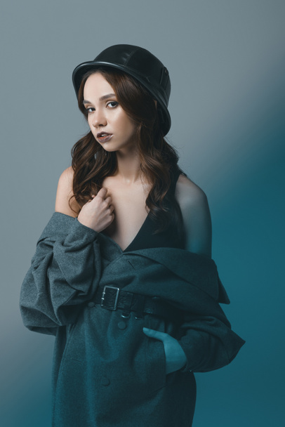 attractive girl posing in autumn coat and military helmet, isolated on grey with blue filter - Photo, Image