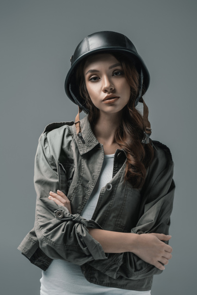 bela menina posando em capacete militar com braços cruzados, isolado em cinza
 - Foto, Imagem