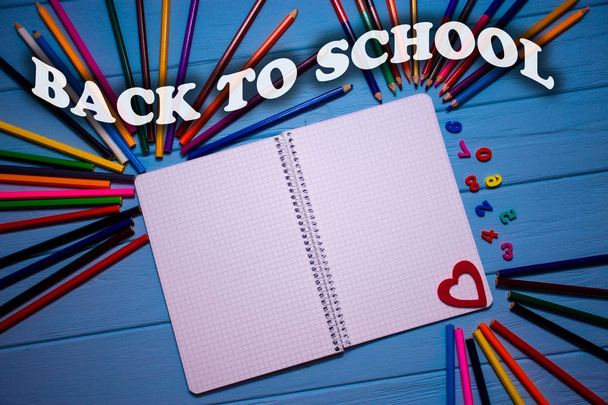 zurück zum Schultext auf hellen Buntstiften auf blauem Holztisch mit weißem Notizbuch. farbenfroher Schulhintergrund - Foto, Bild