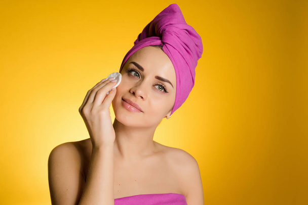attractive young girl with a pink towel on her head cleans her face with a cotton disc - Photo, image