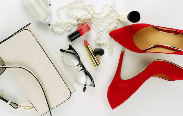 Female fashionable stylish accessories and cosmetics. red shoes with heels, white bag, watch, glasses, lipstick, mascara, red nail polish on a white background. Beauty blog concept. Copy space - 写真・画像