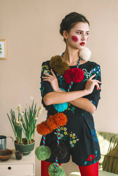 Модная красавица-брюнетка в комбинезоне с цветочной вышивкой с цветным макияжем: красные чики и губы. Стиль бабушки. Ретушированный портрет
 - Фото, изображение