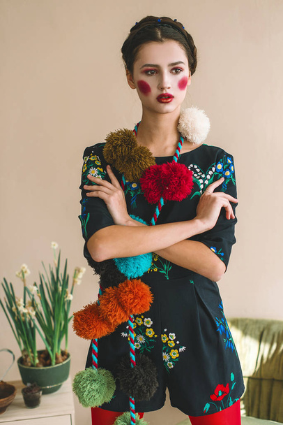 Menina morena bonita na moda em um macacão com bordado floral com maquiagem a cores: bochechas vermelhas e lábios. Avó estilo chique. Retrato retocado
 - Foto, Imagem