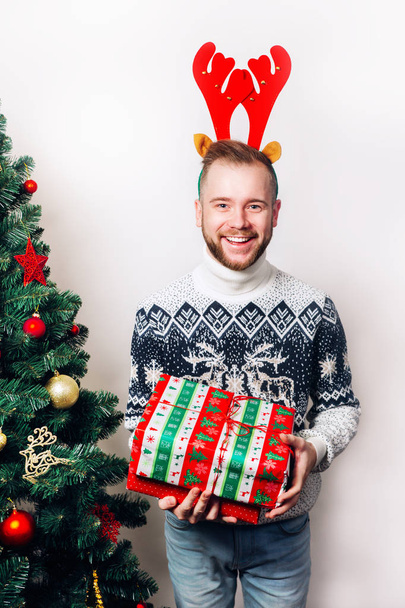 man in sweater holding presents near Christmas tree - Zdjęcie, obraz