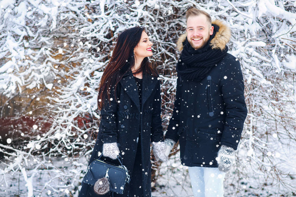 Beautiful young couple holdind each other hand and smiling in snow winter park - Фото, зображення