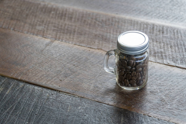 Koffiebonen in glazen flessen met oude houten vloer - Foto, afbeelding