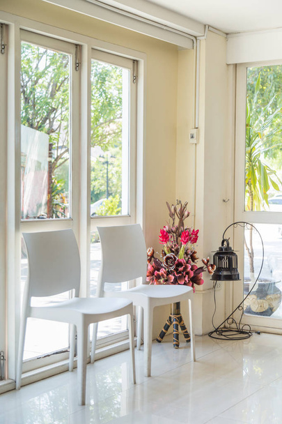 chaises blanches et fleurs artificielles avec lampe par les fenêtres
. - Photo, image