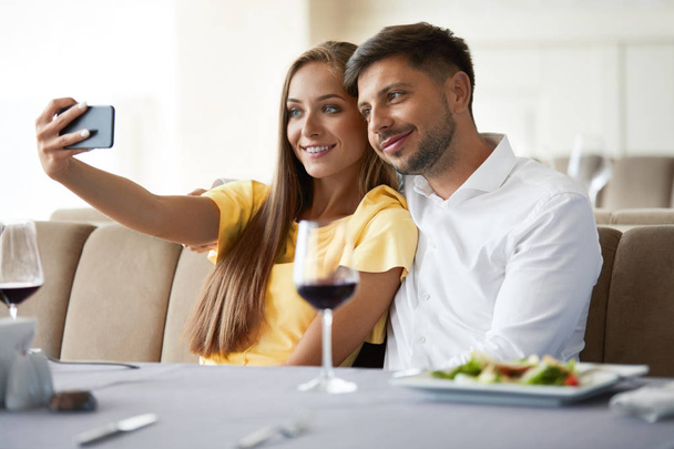 Couple In Restaurant. Couple Taking Photos On Phone. - Foto, Imagen