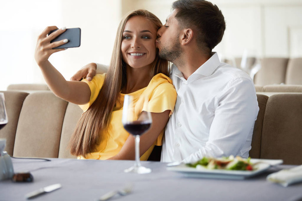 Couple In Restaurant. Couple Taking Photos On Phone. - Фото, изображение