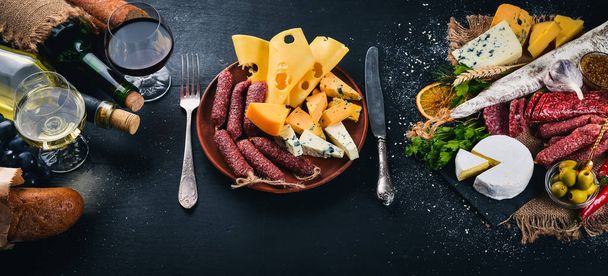 A bottle of wine, cheeses and traditional sausages on a wooden background. Brie cheese, blue cheese, gorgonzola, fuete, salami. Free space for text. Top view. - Фото, зображення