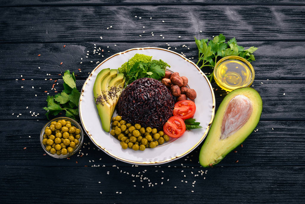 Healthy food. Black rice, avocado, cherry tomatoes, green peas and hazelnut. On a wooden background. Top view. Free space for your text. - Photo, Image