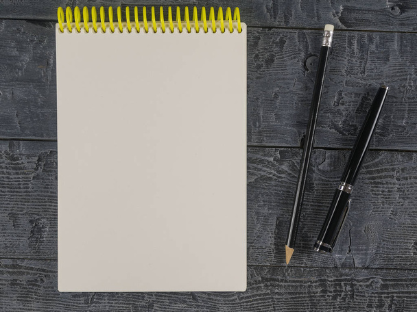 Μαύρη πένα και το μολύβι με μια ανοικτή σημειωματάριο στο μαύρο ξύλινο τραπέζι. Η θέα από την κορυφή. - Φωτογραφία, εικόνα