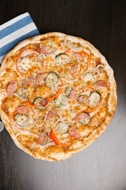 Vista superior da pizza com picles, salsichas, cebolas, pimentas, presunto e queijo
 - Foto, Imagem
