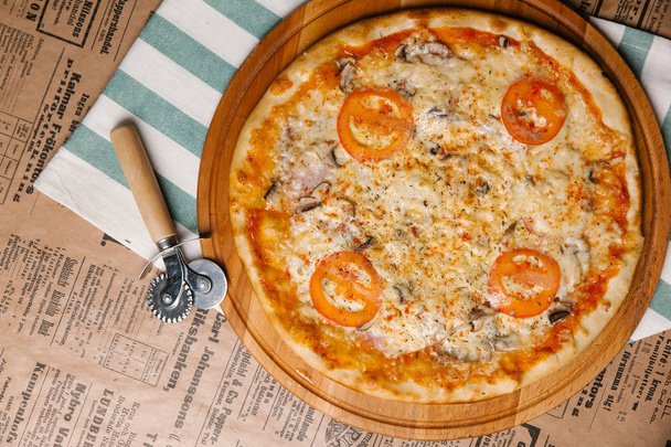 Pizza de queso con tomates, jamón y champiñones servidos en bandeja de madera
 - Foto, Imagen