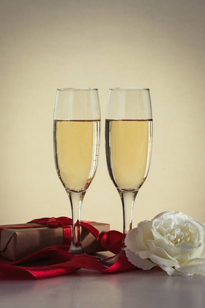Dvě sklenice šampaňského, dárek zabalený a bílé růže toku - Fotografie, Obrázek